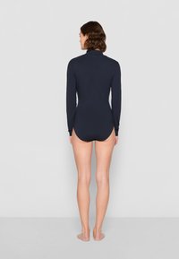 Marineblauwe longsleeve bodysuit met hoge kraag, met een strakke pasvorm en een hoge beenopening aan de achterkant. Glad textuur.