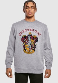 Szary sweter z kolorowym herbem Gryffindoru, z lwem, czerwonymi i złotymi akcentami oraz słowem "GRYFFINDOR" nad emblematem.