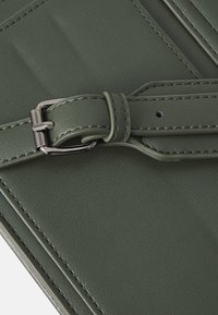 Donkergroen textuurleer met een gladde afwerking, voorzien van een zilveren metalen gesp en gestikte details over het oppervlak.
