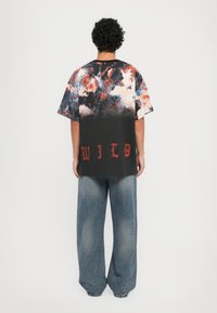 Svart oversized t-skjorte med flerfarget abstrakt trykk, med ordet "WILD" i rød skrift nederst. Løs passform, korte ermer.