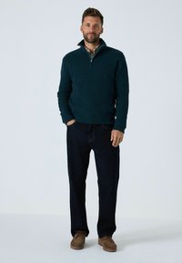 Pulover din fleece de un verde închis cu fermoar pe un sfert, asortat cu blugi drepți de un albastru închis și pantofi negri cu șireturi. Textură netedă.