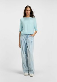 Top azzurro chiaro in maglia con maniche corte, abbinato a jeans larghi in denim chiaro e sneakers bianche. Design semplice con una vestibilità rilassata.