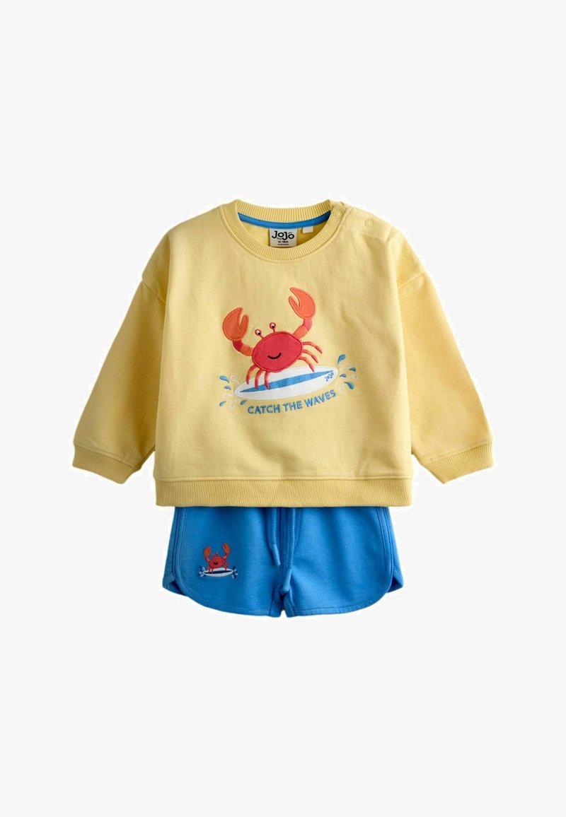 Gul langærmet skjorte med rød krabbe på et surfbræt og teksten "Catch the Waves", kombineret med blå shorts med en lille matchende krabbe.