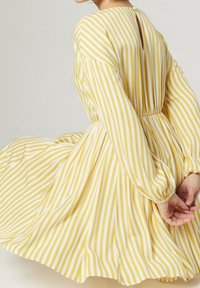 Žluto-bílý pruhovaný celek s dlouhými rukávy, přiléhavým pasem, vysokým výstřihem a detaily s klíčovou dírkou na zadní straně. Volný materiál a skladanou sukni.