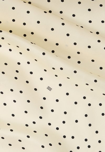 Ύφασμα σε κρεμ απόχρωση με μικρές μαύρες πουά, ομοιόμορφα κατανεμημένες, και διακριτικές πτυχές που δημιουργούν απαλές σκιές.