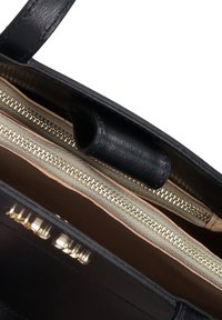 Interno di una borsa in pelle nera con cerniere dorate. Presenta due scomparti e un rivestimento beige a contrasto. Texture liscia in tutta la borsa.