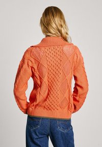 Suéter de punto naranja con cuello alto, que presenta patrones texturizados y formas de diamante, con dobladillo acanalado, mostrado desde la parte trasera.