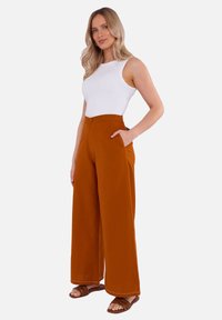 Wijdvallende broek in oranje stof, met een hoge taille, zakken en contrasterende witte stiksels. Gepaard met een strakke witte tanktop.