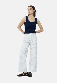 Débardeur navy ajusté et pantalon large avec un motif floral bleu clair. La tenue est complétée par des sandales noires à lanières.