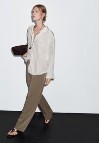 Light beige silk blouse with a collar, paired with olive green wide-leg trousers. Accessory includes a dark brown clutch and strappy sandals.