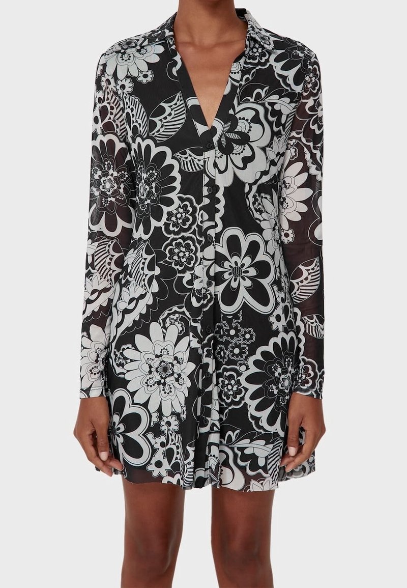 Robe boutonnée à manches longues avec col, motif floral noir et blanc, portée par une personne du cou jusqu'au milieu de la cuisse.