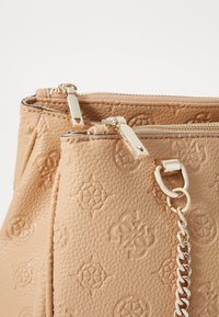 Borsa a mano in pelle beige con texture e motivi in rilievo, dotata di dettagli in oro e una catena decorativa sul lato, chiusura con cerniera nella parte superiore.