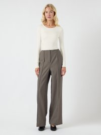Langermet, tettsittende kremfarget topp kombinert med høy i livet, vid buksestil i grått. Merkelig tekstur i stoffet med diskrete folder og glatte svarte sko.
