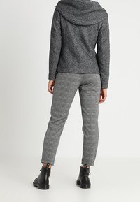 Harmaa huppari pehmeällä pinnalla, yhdistetty harmaisiin kuvioituihin kapealahkeisiin housuihin ja mustiin nilkkureihin, joissa on nauhat.