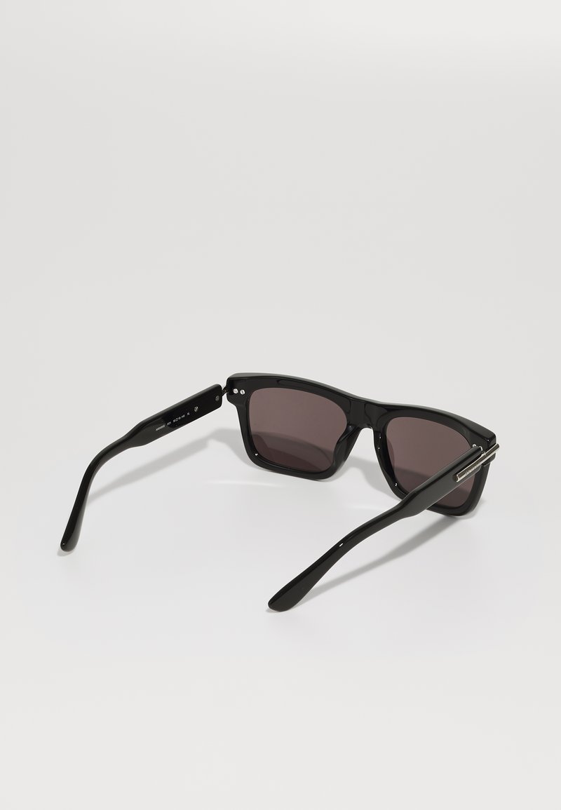 Occhiali da sole rettangolari neri con lenti scure e montatura in plastica lucida. Presentano asticelle eleganti con piccoli dettagli metallici.