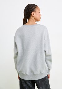 Grijze katoen sweatshirt met een losse pasvorm, brede halslijn en geribbelde manchetten. Opvallend textuur oppervlak en verlaagde schouders. Donkere patroonbroek zichtbaar.