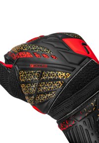Schwarzer und roter Torwarthandschuh mit strukturiertem schwarzem Material, Wabenmustern in Gold und Rot sowie verstellbarem Handgelenkriemen für sicheren Sitz.