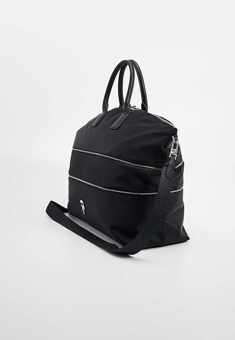Bolsa de viaje de nylon negro con dos asas superiores y una correa para el hombro desmontable. Cuenta con cremalleras plateadas y un detalle del logo en el lateral.