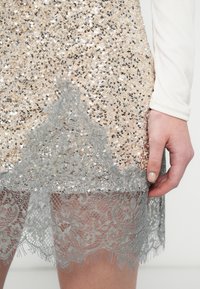 Flitteres ruha arany és ezüst színben. Világosszürke, texturált csipke szegéllyel rendelkezik, amely finom virágmintákat ad az alján.