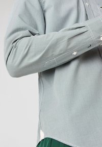 Chemise à boutons à carreaux noir et blanc, avec manches retroussées, ourlet droit et boutons blancs. Le matériau semble lisse avec une légère brillance.