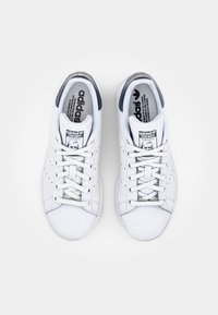 Białe skórzane sneakersy Adidas Stan Smith z ciemnoniebieskimi akcentami, z perforowanymi bokami, płaskimi sznurówkami i logo na języku.