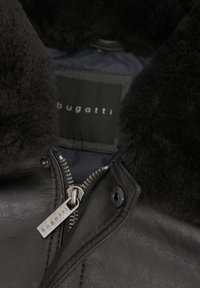 Schwarze Lederjacke mit Shearling-Kragen, Reißverschluss und innen angebrachter „bugatti“-Logoetikette. Glatte Textur und strukturiertes Design.