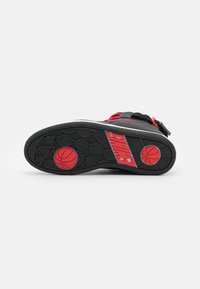 Semelle de chaussure de basket-ball noire avec des accents rouges, présentant un motif d'adhérence hexagonal et un logo de basket-ball rouge. Matériau en caoutchouc durable.