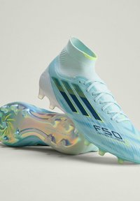 Chaussures de football montantes bleu clair avec semelles cloutées iridescentes, rayures noires et jaunes, et marquage "F50" sur le côté.