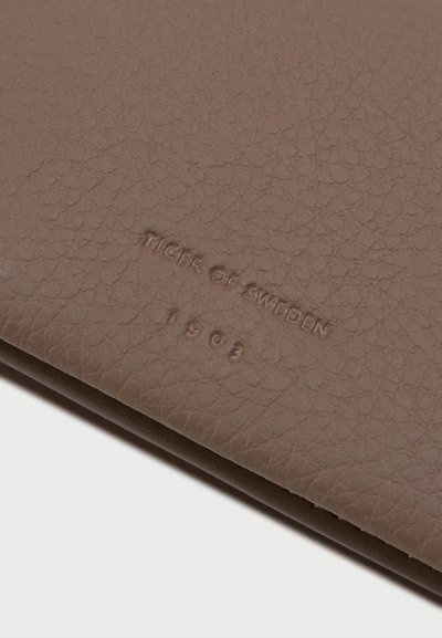 Carteira de couro castanho com acabamento texturizado. Apresenta o nome da marca em relevo "Tiger of Sweden" e o ano "1963."