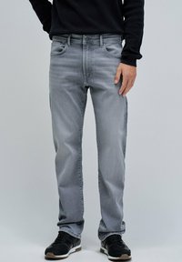 Jeans de mezclilla gris con diseño de cinco bolsillos, corte recto y un desvanecimiento sutil. Combinados con zapatos deportivos negros.