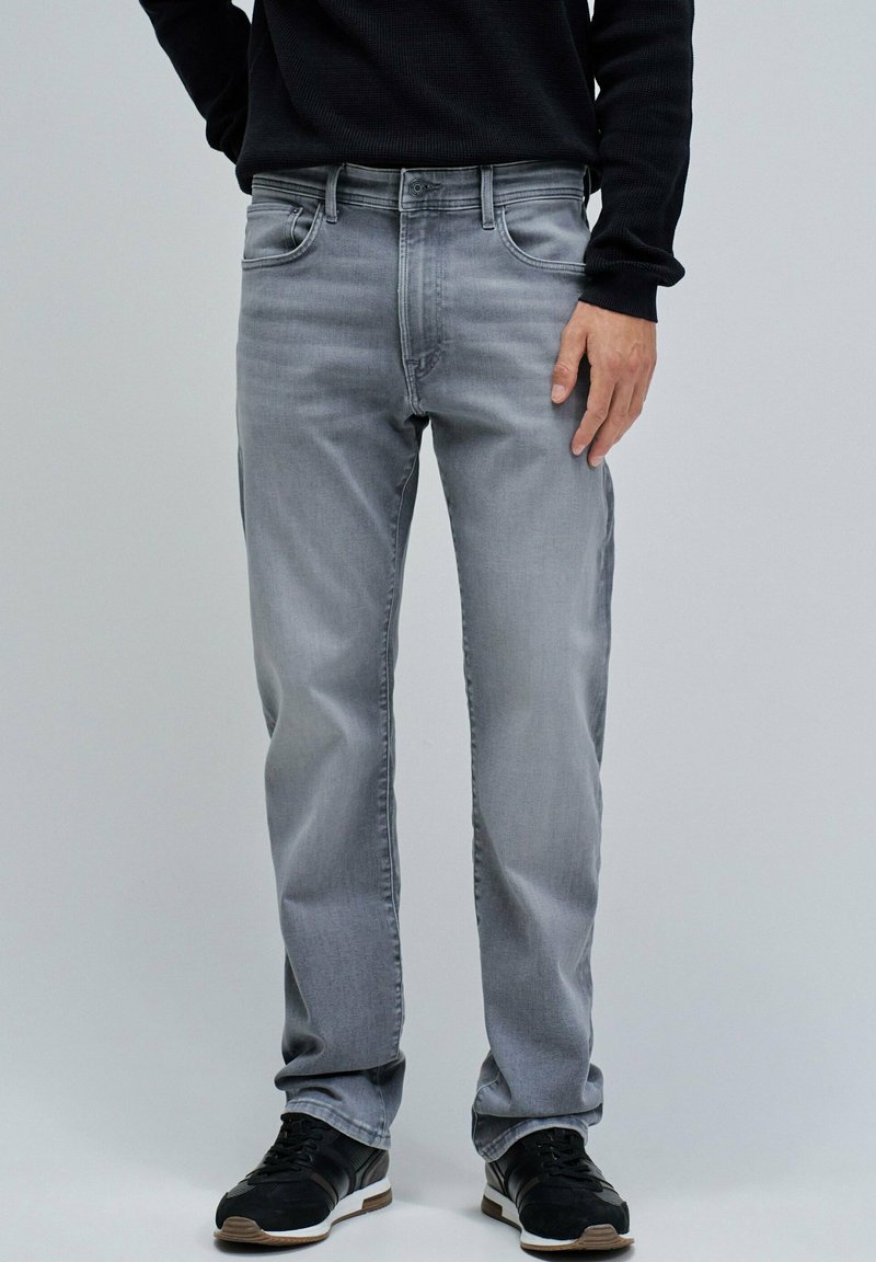 Jeans de mezclilla gris con diseño de cinco bolsillos, corte recto y un desvanecimiento sutil. Combinados con zapatos deportivos negros.