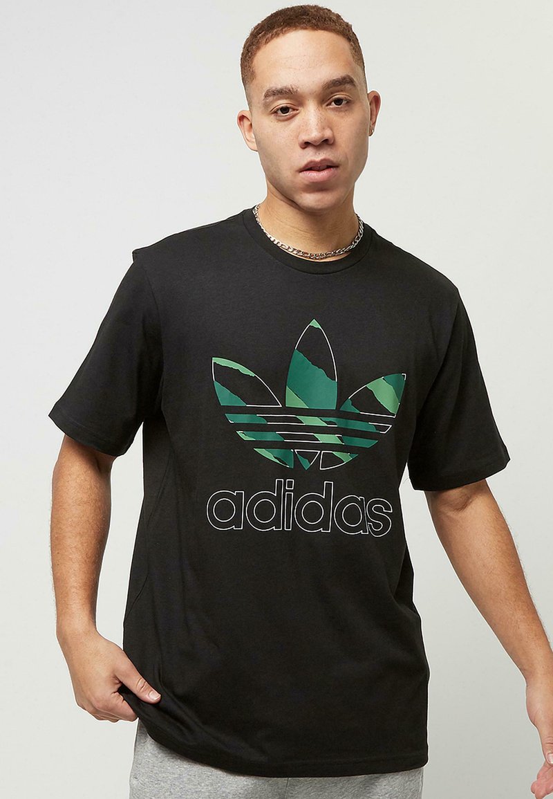 Zwarte ronde hals t-shirt gemaakt van katoen, met een groot groen en zwart camouflaged Adidas trefoil logo en vetgedrukte "adidas" letters in het wit.