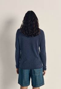 Jūros melsvos ilgomis rankovėmis marškiniai, pagaminti iš minkštos medžiagos, derinami su šviesiai mėlynomis džinsinėmis šortais. Yra apvalus iškirpimas ir laisvas siluetas.