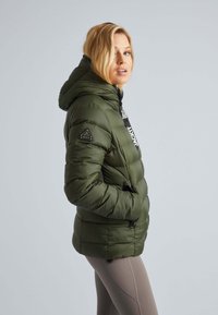 Olijf groene gewatteerde jas met een capuchon, voorzien van een ritssluiting, zijzakken en een logo op de linkermouw.