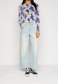 Långärmad topp i en blå, grön och lila tie-dye-mönster; vida ljusblå jeans; svarta högskaftade sneakers.