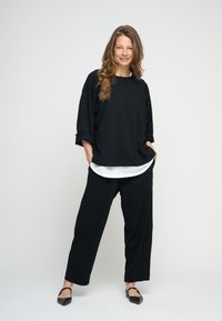 Fekete, túlméretezett hosszú ujjú felső fehér inggel rétegezve, fekete bő szárú nadrággal és hegyes orrú lapos cipővel párosítva. Sima anyag minimális díszítéssel.