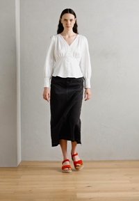 Blouse blanche à manches bouffantes longues, jupe midi en denim noir et sandales rouges à semelle épaisse. Texture lisse et design simple.