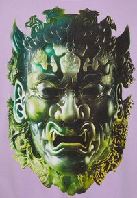 Grafica verde e nera di una maschera feroce e ornata con caratteristiche pronunciate, denti aguzzi e dettagli intricati su uno sfondo lilla chiaro.