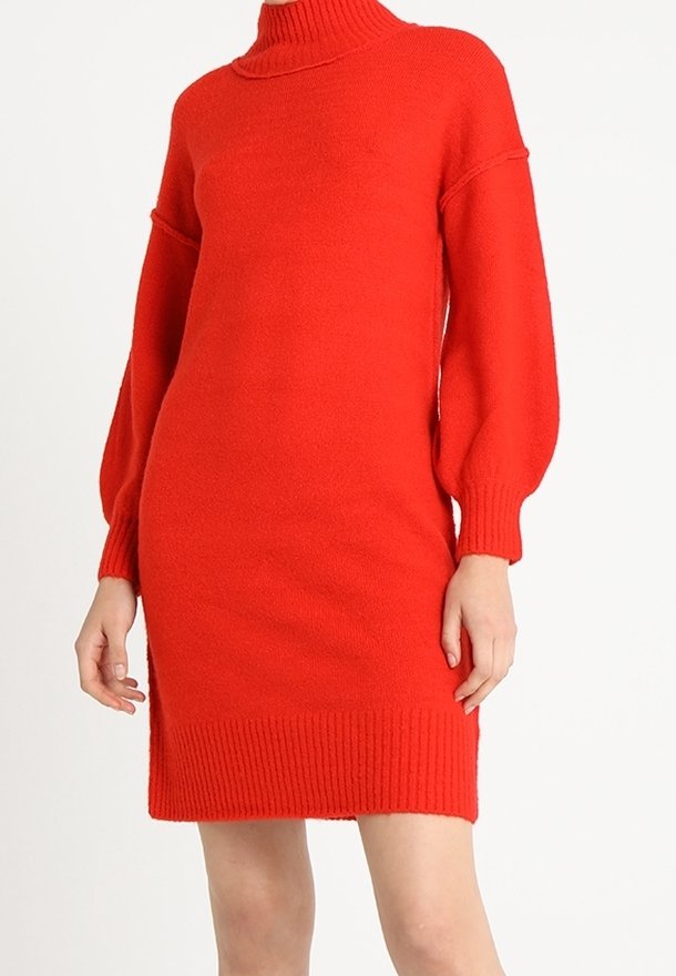 Robe rouge tricotée à manches longues avec un col roulé et des poignets et ourlet côtelés, portée par une personne debout devant un fond blanc uni.
