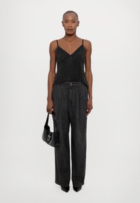 Camiseta sin mangas negra con lunares, combinada con pantalones sueltos gris oscuro. Incluye un bolso negro y tacones de punta. Texturas suaves, diseño minimalista.