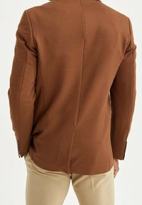 Bruine gestructureerde jas met een textuur en een strak ontwerp, voorzien van een enkele split aan de achterkant en gedetailleerde knoopaccenten op de manchetten.