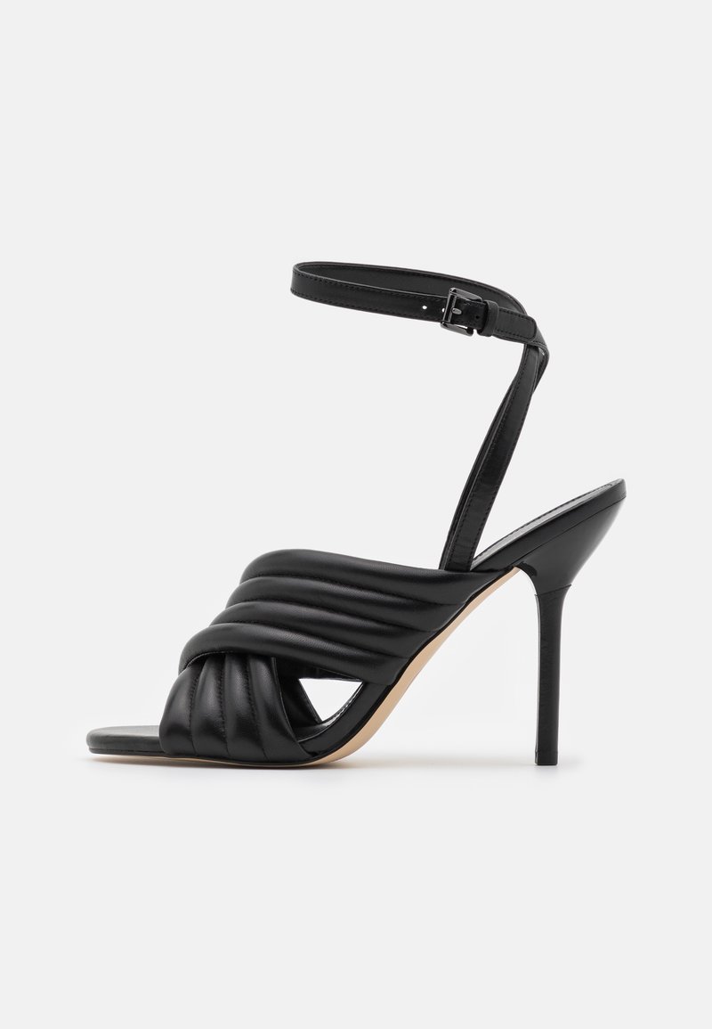Sandale noire à talons hauts avec des brides avant tressées et rembourrées, et une lanière fine à la cheville avec fermeture à boucle.