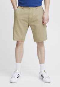Kaki shorts laget av lett stoff, med flat front, beltehemper og sidelommer. Kombinert med hvite sokker og joggesko.