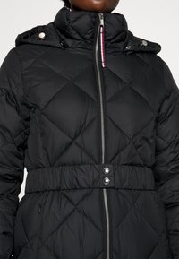 Sort quiltet pufferjakke med høj krave, indsnævret talje og metalliske detaljer. Har en frontlynlås og trykknapdetaljer.