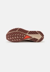 Semelle de chaussure avec bande de roulement en caoutchouc marron et beige, motif de grip texturé, et un détail triangulaire orange au centre.