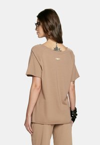 Brązowy t-shirt z krótkim rękawem i szerokim dekoltem, z małą metkę z tyłu. Miękka tkanina i luźny krój.