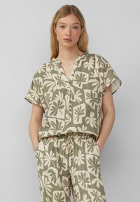Kurzärmlige, kragenlose Bluse in Olivgrün mit cremefarbenem Blumenmuster; leichtes, strukturiertes Gewebe; kombiniert mit passender Hose mit elastischem Bund.