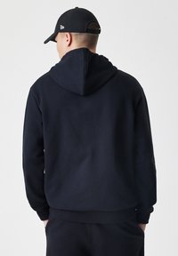 Hoodie bleu marine avec capuche à cordon, poignets et ourlet côtelés. Porté avec un ensemble assorti, montrant une texture en coton lisse et un design décontracté.