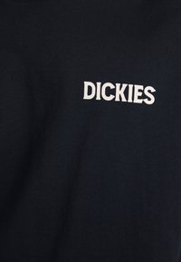 Camiseta de color azul marino hecha de algodón, con mangas cortas, que presenta un logo bordado en blanco de "DICKIES" en la parte superior izquierda.
