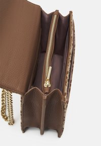 Sac à main en cuir brun texturé avec une fermeture éclair dorée, comportant deux compartiments et une bandoulière en chaîne. L'intérieur est doté d'une doublure lisse.